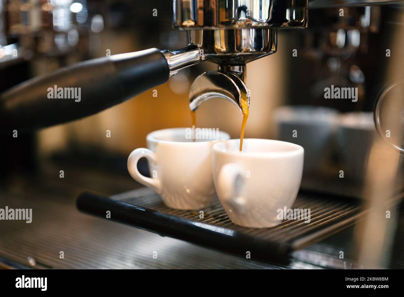 Il caffè espresso scorre da una macchina da caffè portafiltro in due tazze bianche. Foto Stock