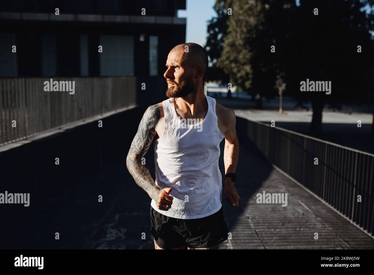 Uomo tatuato barbuto che fa jogging all'aperto, ritratto di atletico che fa allenamento cardio in città Foto Stock