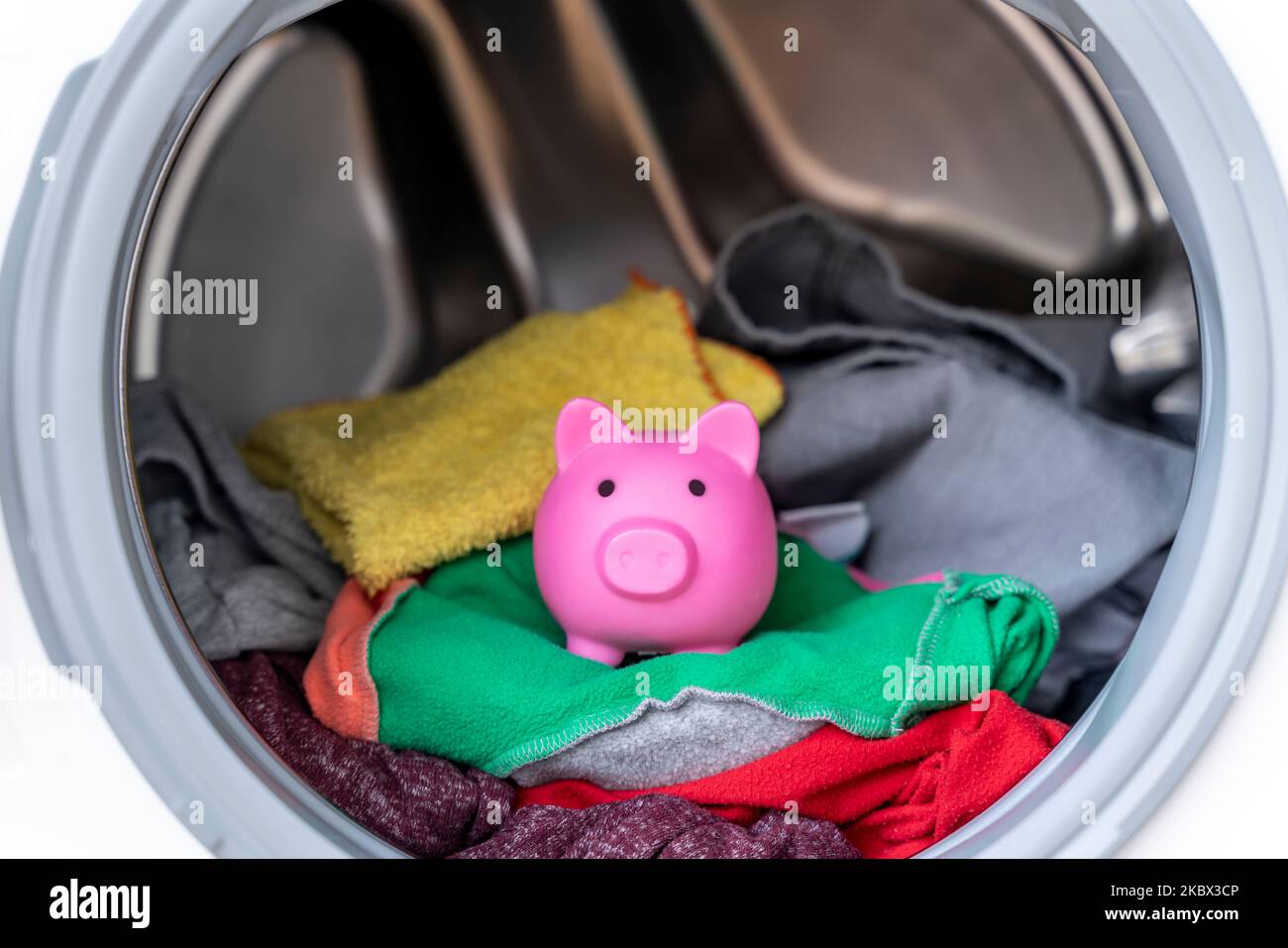 Concetto di risparmio di energia elettrica con una lavatrice con una banca di porcellini all'interno Foto Stock