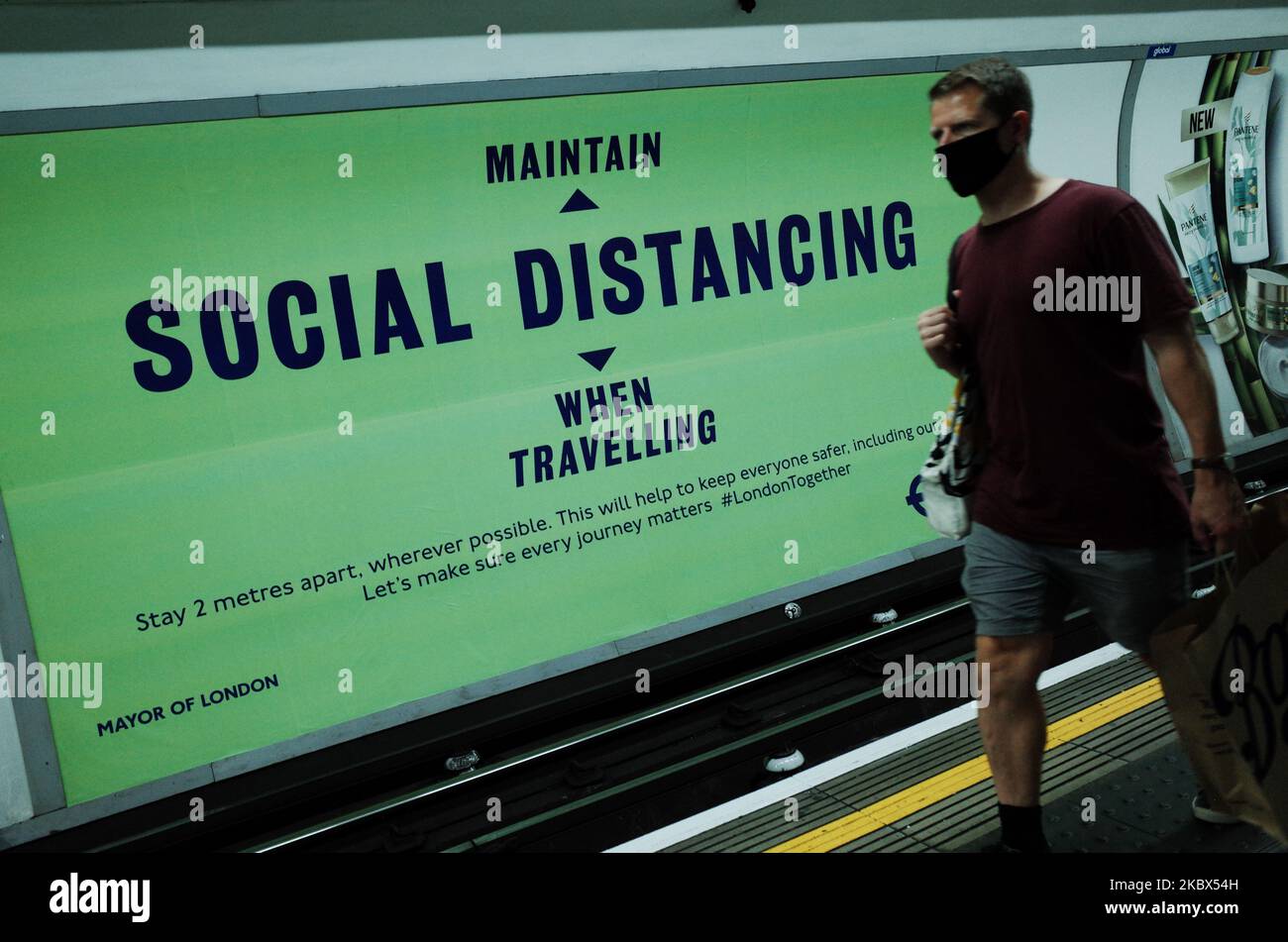 Un uomo che indossa una maschera facciale, attualmente incaricato dei trasporti pubblici, passa un poster che ricorda ai passeggeri la necessità di un allontanamento sociale su una piattaforma Northern line alla stazione di Tottenham Court Road a Londra, Inghilterra, il 14 agosto 2020. Il numero di passeggeri della metropolitana di Londra rimane ben al di sotto dei livelli pre-pandemici, mentre la città continua la sua esitazione dal blocco del coronavirus, con i timori del covid-19 che ancora oggi molti non utilizzano i trasporti pubblici. (Foto di David Cliff/NurPhoto) Foto Stock