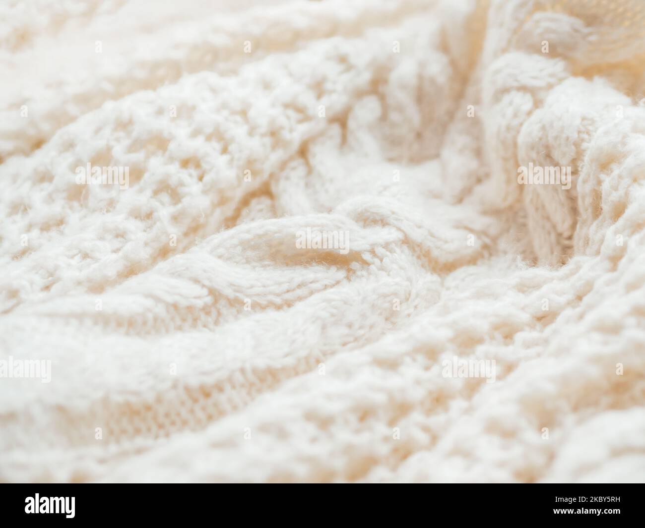 Maglione a maglia a cavo realizzato a mano. Texture di tessuto caldo lavorato a maglia con motivo. Cardigan bianco sbriciolato. Intimo vestito autunnale per un clima sereno. Foto Stock