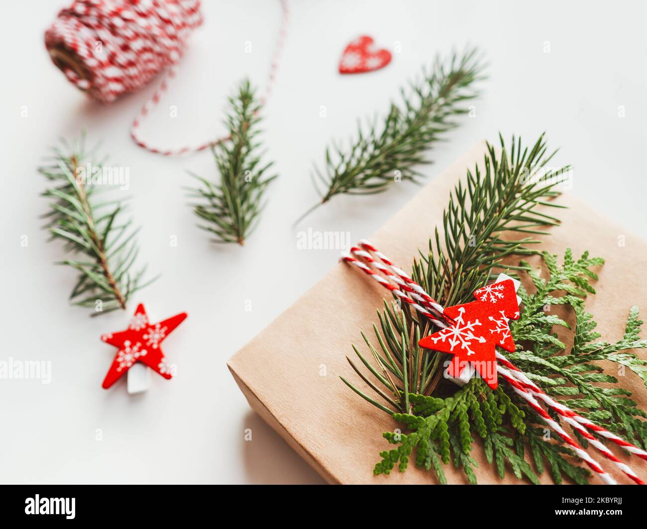 Regali natalizi avvolti in carta artigianale con rami di abete. Decorazioni rosse a forma di albero di Natale. Regali di Capodanno. Sfondo festivo. Foto Stock