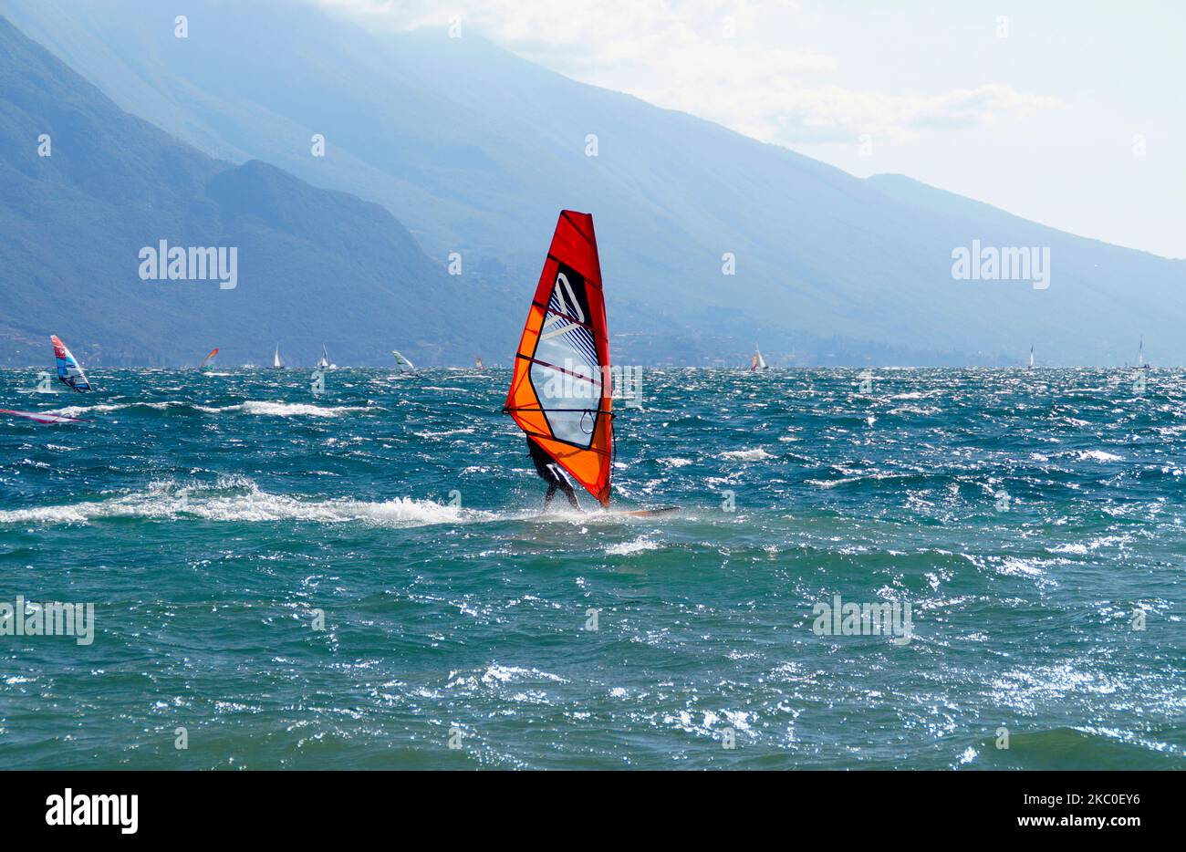 Un surfista windsurf sul lago di Garda presso la città mediterranea Riva del Garda con le montagne sullo sfondo, Lombardia, Italia settentrionale Foto Stock