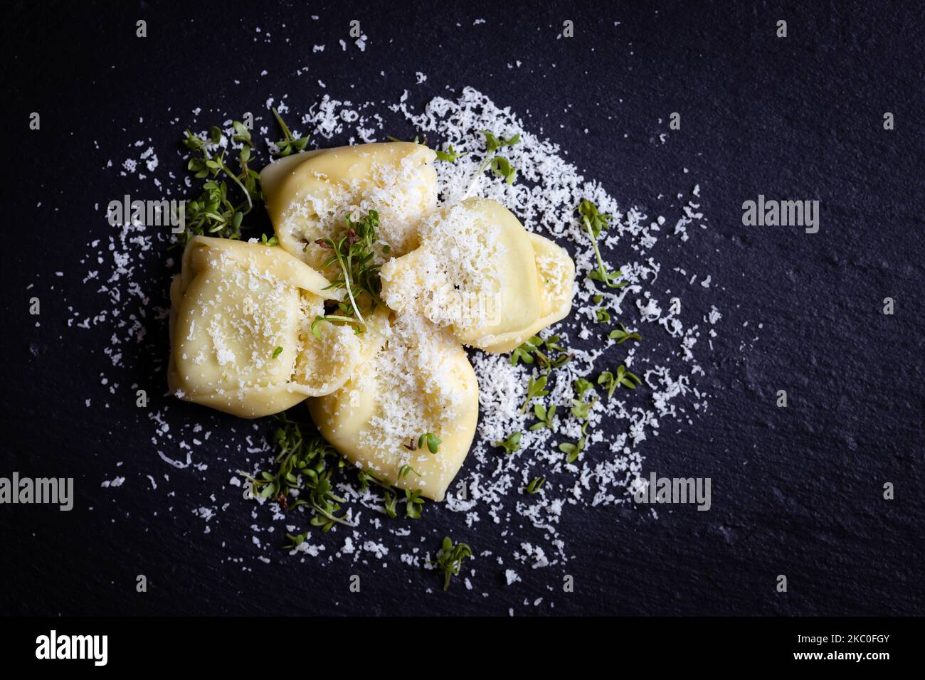 Tortellini con parmigiano su sfondo nero, fotografati dall'alto Foto Stock