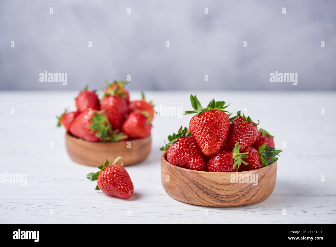 Fragole fresche mature in ciotole di legno su un tavolo di legno bianco. Sfondo grigio. Orizzontale, spazio di copia, primo piano. Foto Stock