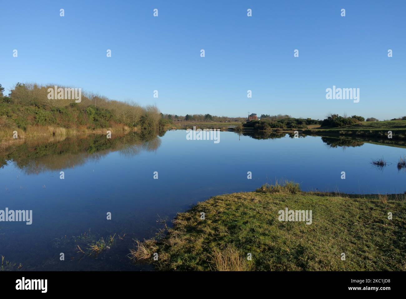 Una giornata invernale brillante con una superficie d'acqua liscia a specchio sui laghi formatisi nella riserva naturale sul campo d'aviazione in disuso a Greenham Common Airbase nea Foto Stock