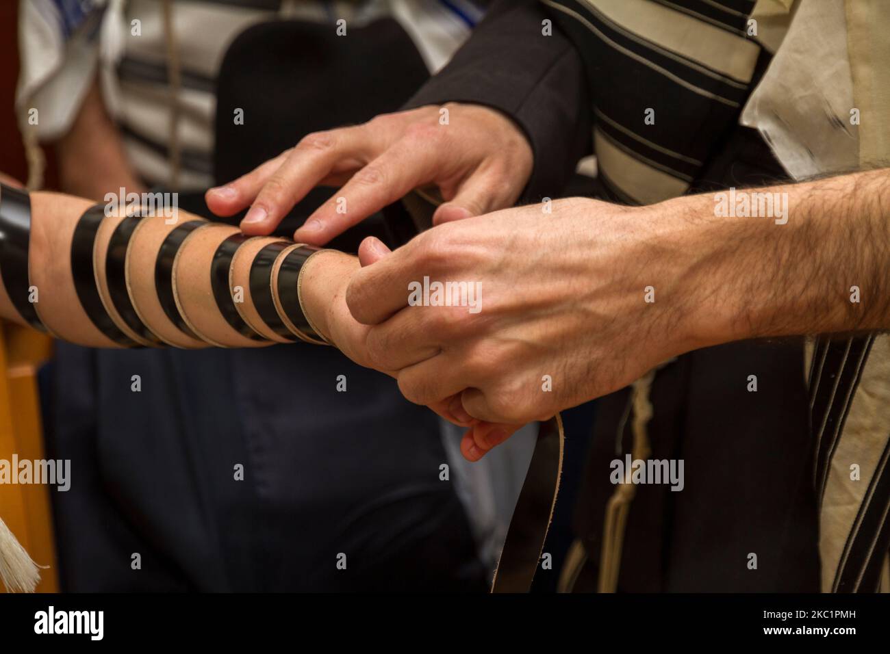 Un uomo ortodosso, indossando uno scialle di preghiera, mise un tefillin  ebraico su Un braccio di un giovane uomo che si preparava alla preghiera,  come parte di un rituale ebraico, la cerimonia