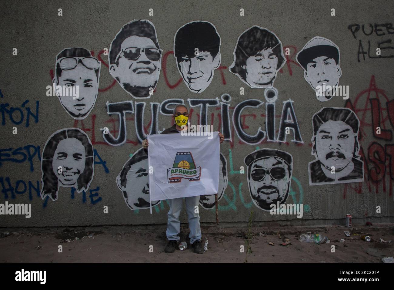 Una persona possiede un flag con un -A- in riferimento a -APRUEBO- (Approve). Proprio di fronte a un murale con foto delle vittime fatali di abusi della polizia durante l'epidemia sociale, con la parola -JUSTICIA- (giustizia) nel centro. Due settimane dopo il plebiscito per respingere o approvare una nuova costituzione politica in Cile nel mezzo della manifestazione e della protesta contro il governo di Sebastián Piñera, la disuguaglianza sociale e il sistema neoliberale. Il 16 ottobre 2020 a Santiago del Cile, Cile. (Foto di Claudio Abarca Sandoval/NurPhoto) Foto Stock