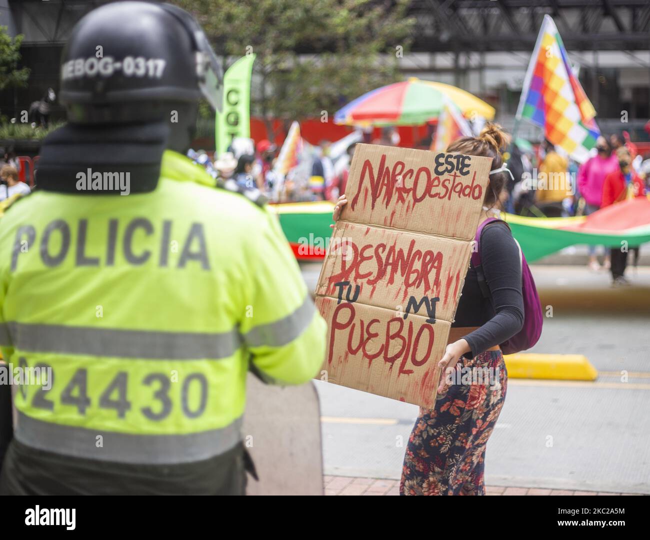 Una donna ha in mano un segno che dice "Stato Narco, sanguina il tuo popolo" di fronte a un poliziotto nella protesta contro il governo nazionale e respingendo i massacri e l'assassinio di leader sociali a Bogotà, in Colombia, il 21 ottobre 2020. (Foto di Daniel Garzon Herazo/NurPhoto) Foto Stock