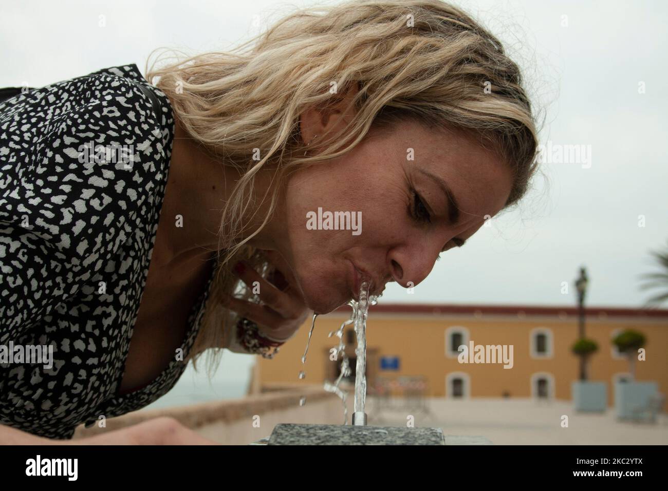 donna bionda che beve acqua cristallina da una fontana a getto Foto Stock