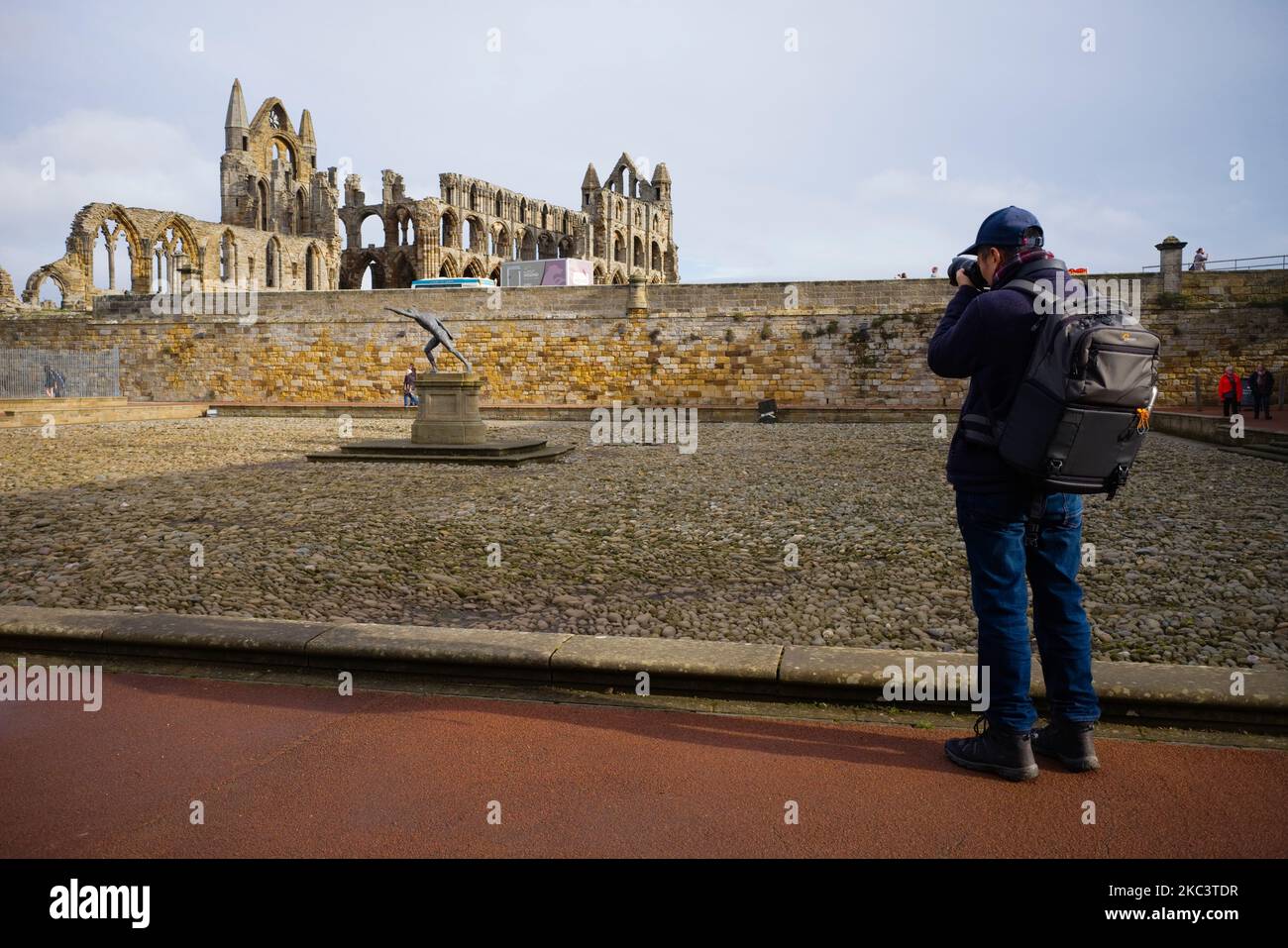 Un fotografo asiatico con una pesante borsa di attrezzature scatta una foto all'Abbazia di Whitby durante il fine settimana Foto Stock