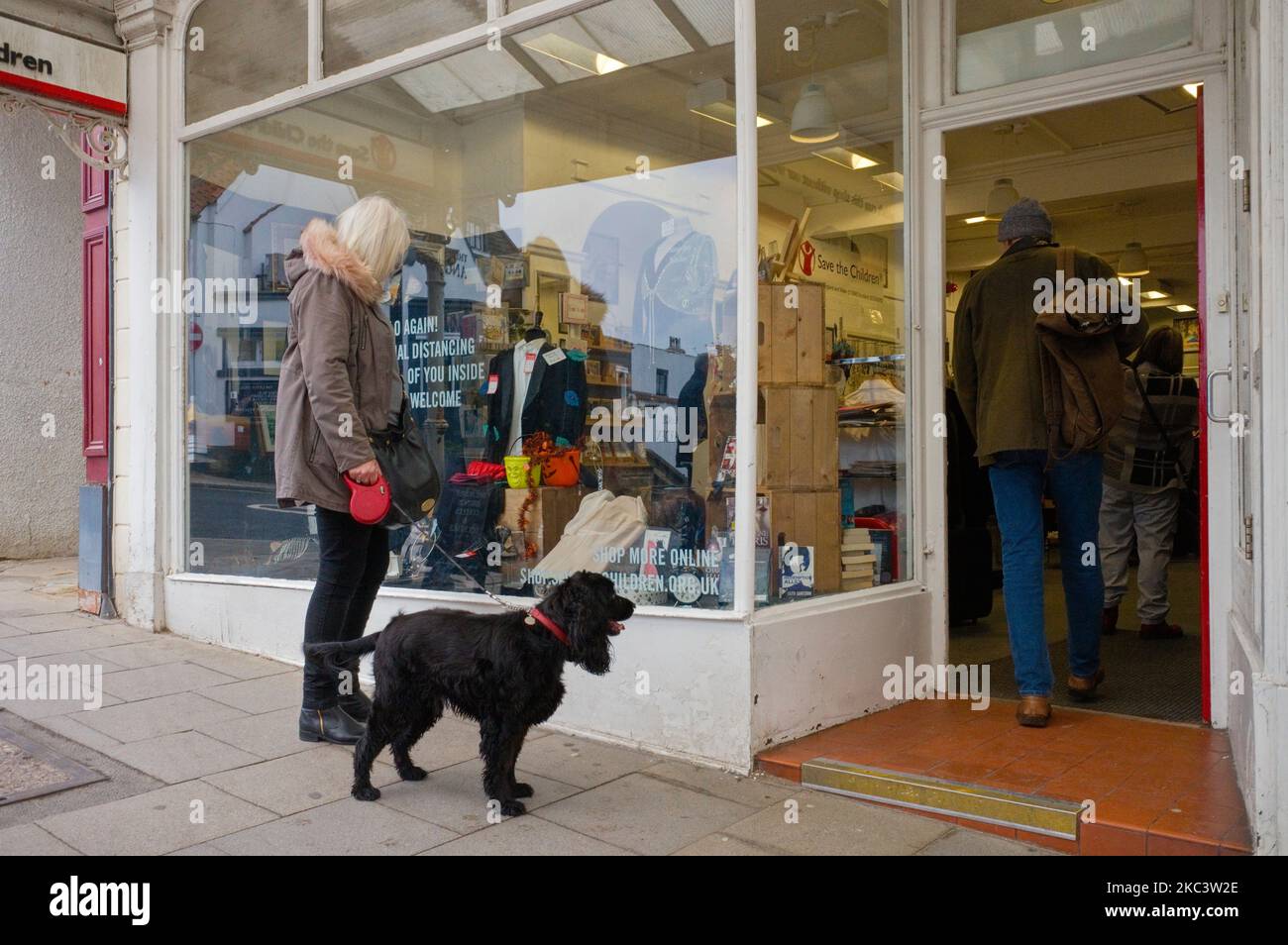 Donna in piedi fuori un negozio di beneficenza con un cane a Flowergate, Whitby Foto Stock