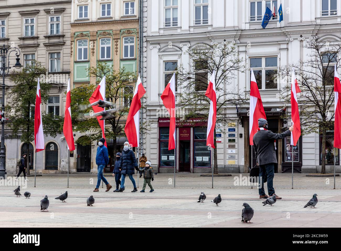La famiglia in maschere protettive si vede camminare di fronte alle bandiere nazionali polacche sulla piazza del mercato principale, mentre la Polonia celebra la sua Giornata dell'Indipendenza nella città vecchia di Cracovia, in Polonia, il 11 novembre 2020. Il mercato principale di Cracovia è di solito pieno di turisti, ma oggi rimane in gran parte vuoto, poiché il turismo globale è diminuito a causa della pandemia di Covid-19. (Foto di Dominika Zarzycka/NurPhoto) Foto Stock