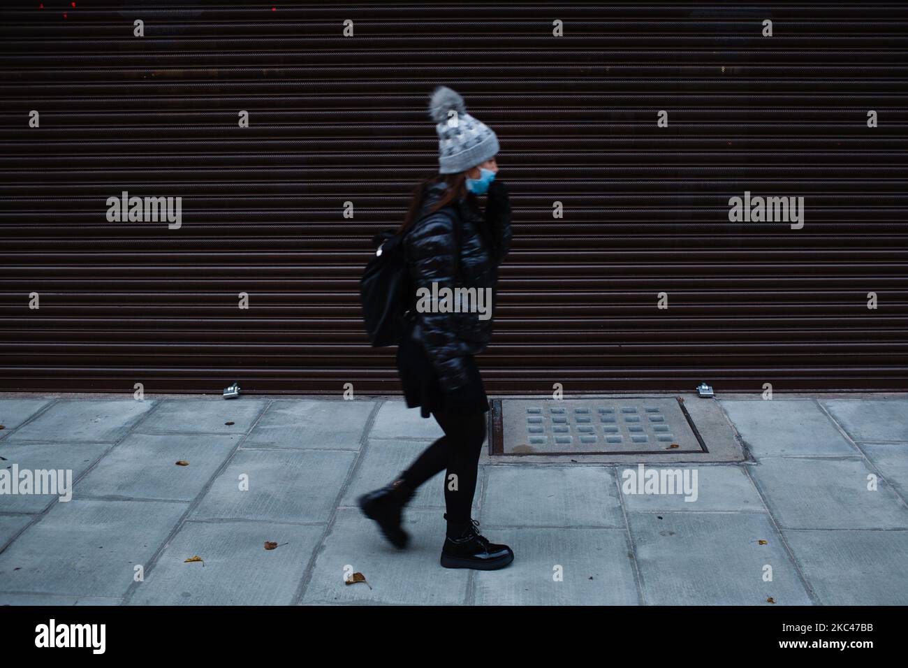 Una donna che indossa una maschera facciale passa davanti a un ramo temporaneamente chiuso e chiuso del gioielliere Ernest Jones su una tranquilla Oxford Street a Londra, Inghilterra, il 18 novembre 2020. In tutta l'Inghilterra negozi non essenziali, bar, ristoranti e altre aziende del settore alberghiero rimangono chiusi come parte del secondo blocco nazionale del coronavirus, iniziato il 5 novembre e in scadenza il 2 dicembre. Il primo ministro britannico Boris Johnson, che ha indicato di non voler estendere il blocco, nel frattempo rimane in isolamento a Downing Street dopo essere venuto in contatto con una M. Foto Stock