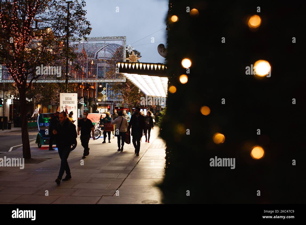 La gente passa davanti alle luci di Natale fuori dai grandi magazzini Selfridges temporaneamente chiusi in una tranquilla Oxford Street a Londra, Inghilterra, il 18 novembre 2020. In tutta l'Inghilterra negozi non essenziali, bar, ristoranti e altre aziende del settore alberghiero rimangono chiusi come parte del secondo blocco nazionale del coronavirus, iniziato il 5 novembre e in scadenza il 2 dicembre. Il primo ministro britannico Boris Johnson, che ha indicato di non voler estendere il blocco, nel frattempo rimane in isolamento a Downing Street dopo essere venuto in contatto con un deputato giovedì scorso w Foto Stock