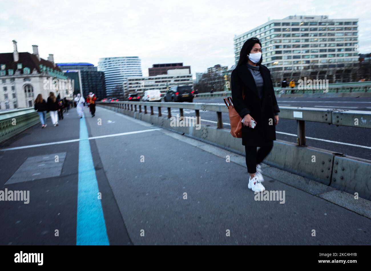 Una donna che indossa una maschera facciale cammina attraverso il Westminster Bridge a Londra, Inghilterra, il 23 novembre 2020. In tutta l'Inghilterra negozi non essenziali, bar, ristoranti e altre aziende del settore alberghiero rimangono chiusi come parte del secondo blocco nazionale del coronavirus, iniziato il 5 novembre e in scadenza il 2 dicembre. (Foto di David Cliff/NurPhoto) Foto Stock