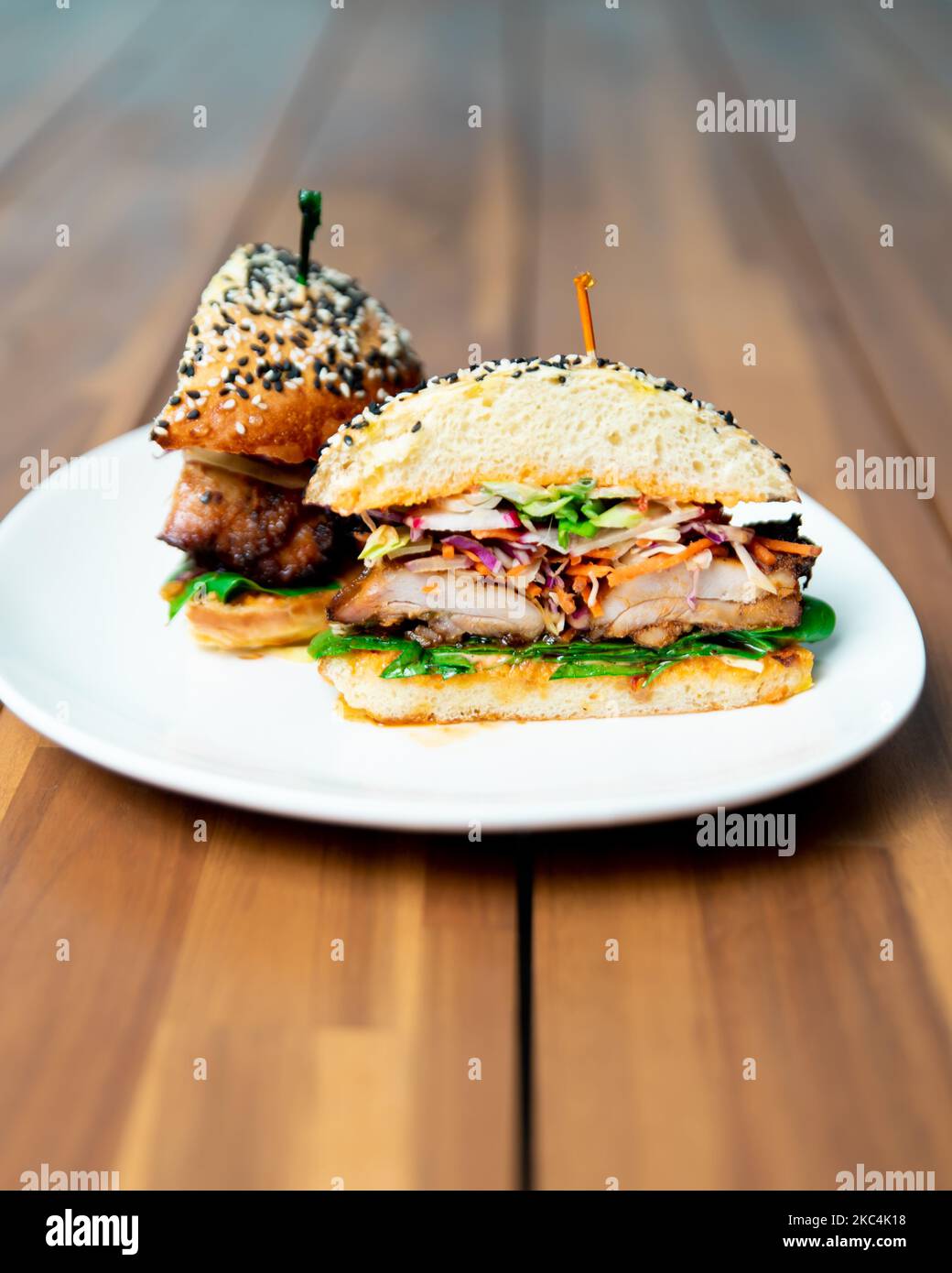 Un primo piano di un delizioso hamburger affettato a metà su un piatto bianco su un tavolo di legno in un ristorante Foto Stock