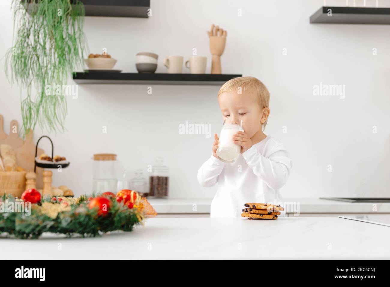 Mattina di Natale. Un bambino si sveglia e beve latte e biscotti di Natale in cucina Foto Stock