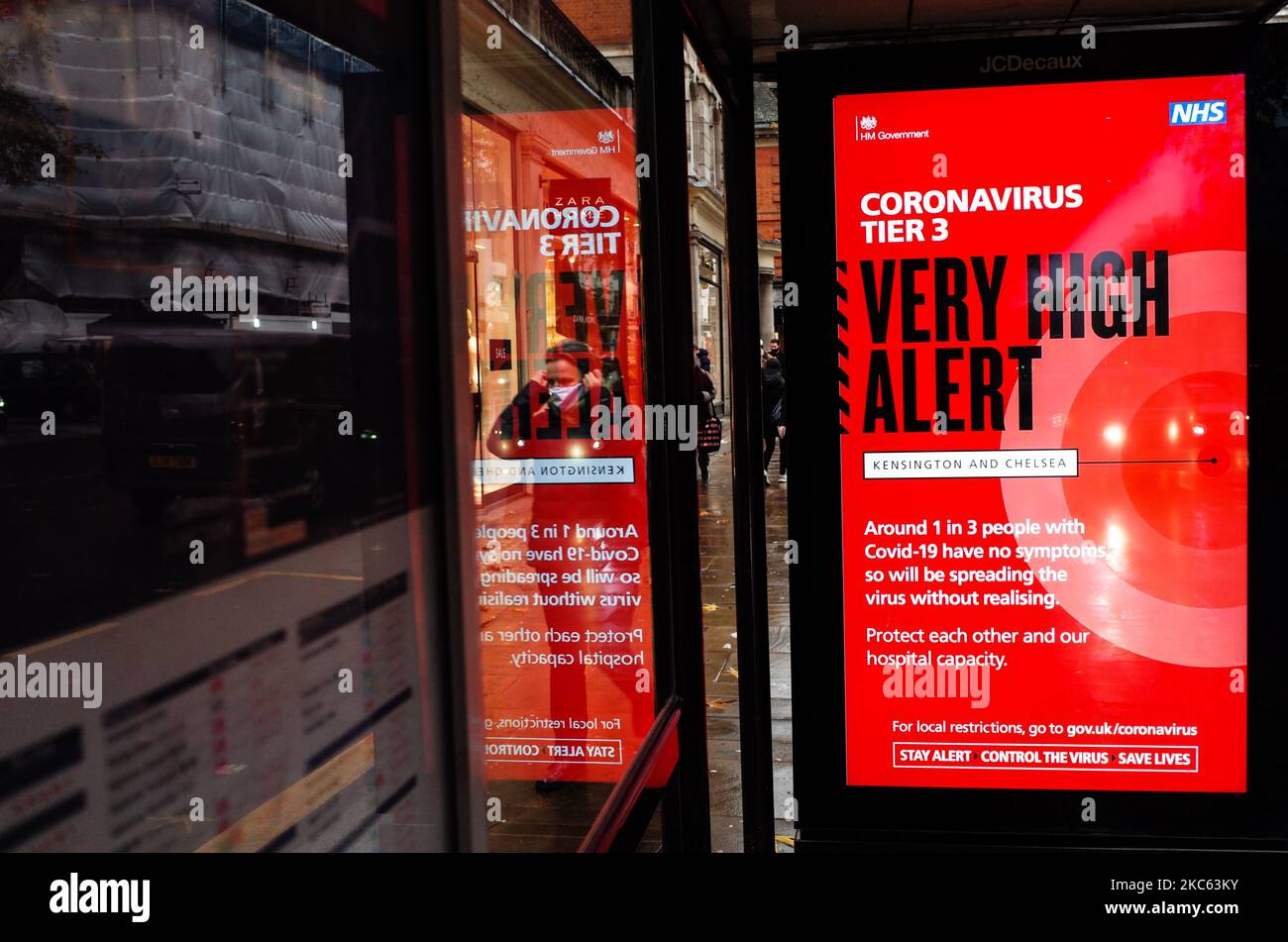 Una donna che indossa una maschera facciale passa oltre un avviso per 'Tier 3' o 'molto alto' restrizioni di allarme coronavirus visualizzato sullo schermo di pubblicità digitale di una fermata di autobus su Kensington High Street a Londra, Inghilterra, il 18 dicembre 2020. Le restrizioni di livello 3 sono iniziate a Londra il mercoledì tra le preoccupazioni delle autorità per l'aumento dei numeri covid-19 test positivi in città. I negozi possono rimanere aperti nelle aree di livello 3, ma le aziende del settore alberghiero sono limitate solo ai servizi di asporto e consegna e i luoghi di intrattenimento, inclusi teatri e cinema, devono essere chiusi. (Foto di David Cliff/NurPhoto) Foto Stock