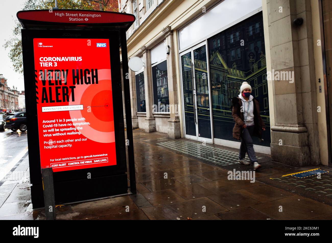 Una donna che indossa una maschera facciale passa oltre un avviso per 'Tier 3' o 'molto alto' restrizioni di allarme coronavirus visualizzato sullo schermo di pubblicità digitale di una fermata di autobus su Kensington High Street a Londra, Inghilterra, il 18 dicembre 2020. Le restrizioni di livello 3 sono iniziate a Londra il mercoledì tra le preoccupazioni delle autorità per l'aumento dei numeri covid-19 test positivi in città. I negozi possono rimanere aperti nelle aree di livello 3, ma le aziende del settore alberghiero sono limitate solo ai servizi di asporto e consegna e i luoghi di intrattenimento, inclusi teatri e cinema, devono essere chiusi. (Foto di David Cliff/NurPhoto) Foto Stock