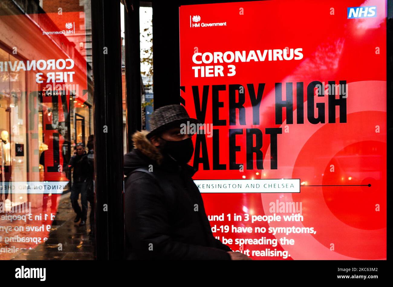 Un uomo che indossa una maschera facciale attende accanto a un avviso per 'Tier 3' o 'molto alto' restrizioni di allarme coronavirus visualizzati sullo schermo di pubblicità digitale di una fermata di autobus su Kensington High Street a Londra, Inghilterra, il 18 dicembre 2020. Le restrizioni di livello 3 sono iniziate a Londra il mercoledì tra le preoccupazioni delle autorità per l'aumento dei numeri covid-19 test positivi in città. I negozi possono rimanere aperti nelle aree di livello 3, ma le aziende del settore alberghiero sono limitate solo ai servizi di asporto e consegna e i luoghi di intrattenimento, inclusi teatri e cinema, devono essere chiusi. (Foto di David Cliff/NurPhoto) Foto Stock