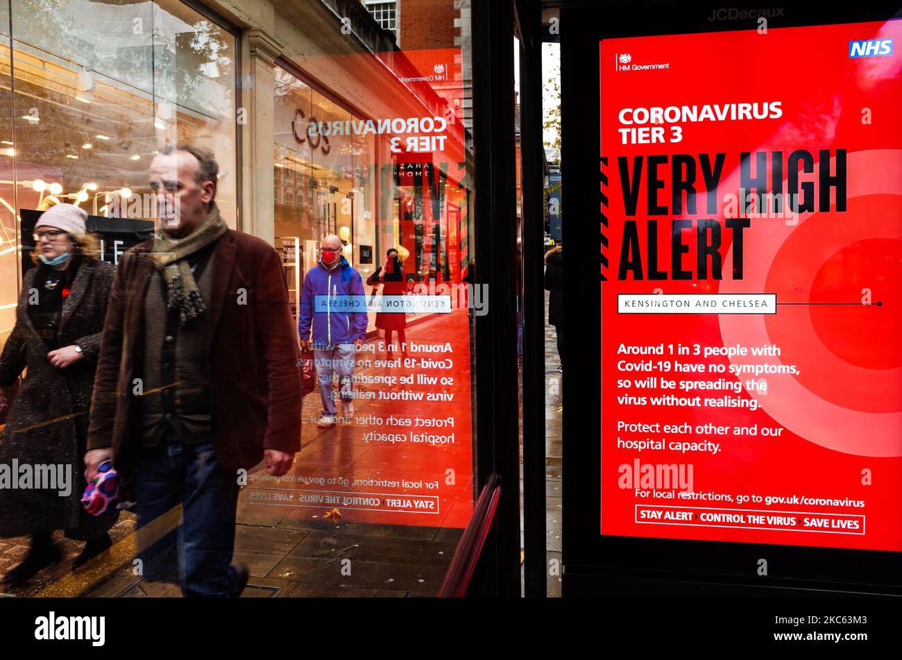 Le persone passano oltre un avviso per 'Tier 3' o 'molto alto' avviso coronavirus restrizioni visualizzate sullo schermo di pubblicità digitale di una fermata di autobus su Kensington High Street a Londra, Inghilterra, il 18 dicembre 2020. Le restrizioni di livello 3 sono iniziate a Londra il mercoledì tra le preoccupazioni delle autorità per l'aumento dei numeri covid-19 test positivi in città. I negozi possono rimanere aperti nelle aree di livello 3, ma le aziende del settore alberghiero sono limitate solo ai servizi di asporto e consegna e i luoghi di intrattenimento, inclusi teatri e cinema, devono essere chiusi. (Foto di David Cliff/NurPhoto) Foto Stock