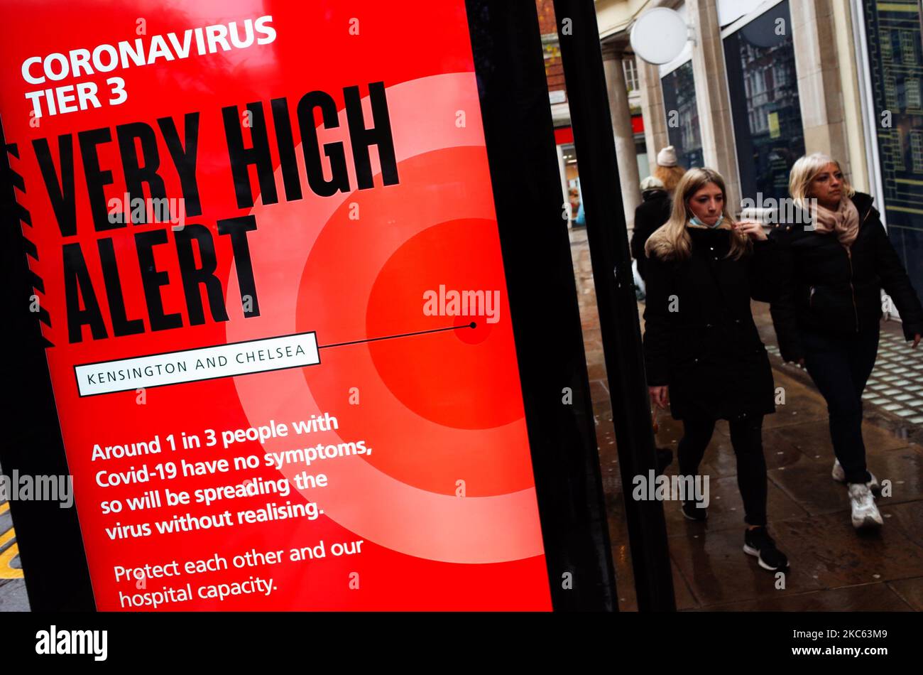 Le persone passano oltre un avviso per 'Tier 3' o 'molto alto' avviso coronavirus restrizioni visualizzate sullo schermo di pubblicità digitale di una fermata di autobus su Kensington High Street a Londra, Inghilterra, il 18 dicembre 2020. Le restrizioni di livello 3 sono iniziate a Londra il mercoledì tra le preoccupazioni delle autorità per l'aumento dei numeri covid-19 test positivi in città. I negozi possono rimanere aperti nelle aree di livello 3, ma le aziende del settore alberghiero sono limitate solo ai servizi di asporto e consegna e i luoghi di intrattenimento, inclusi teatri e cinema, devono essere chiusi. (Foto di David Cliff/NurPhoto) Foto Stock