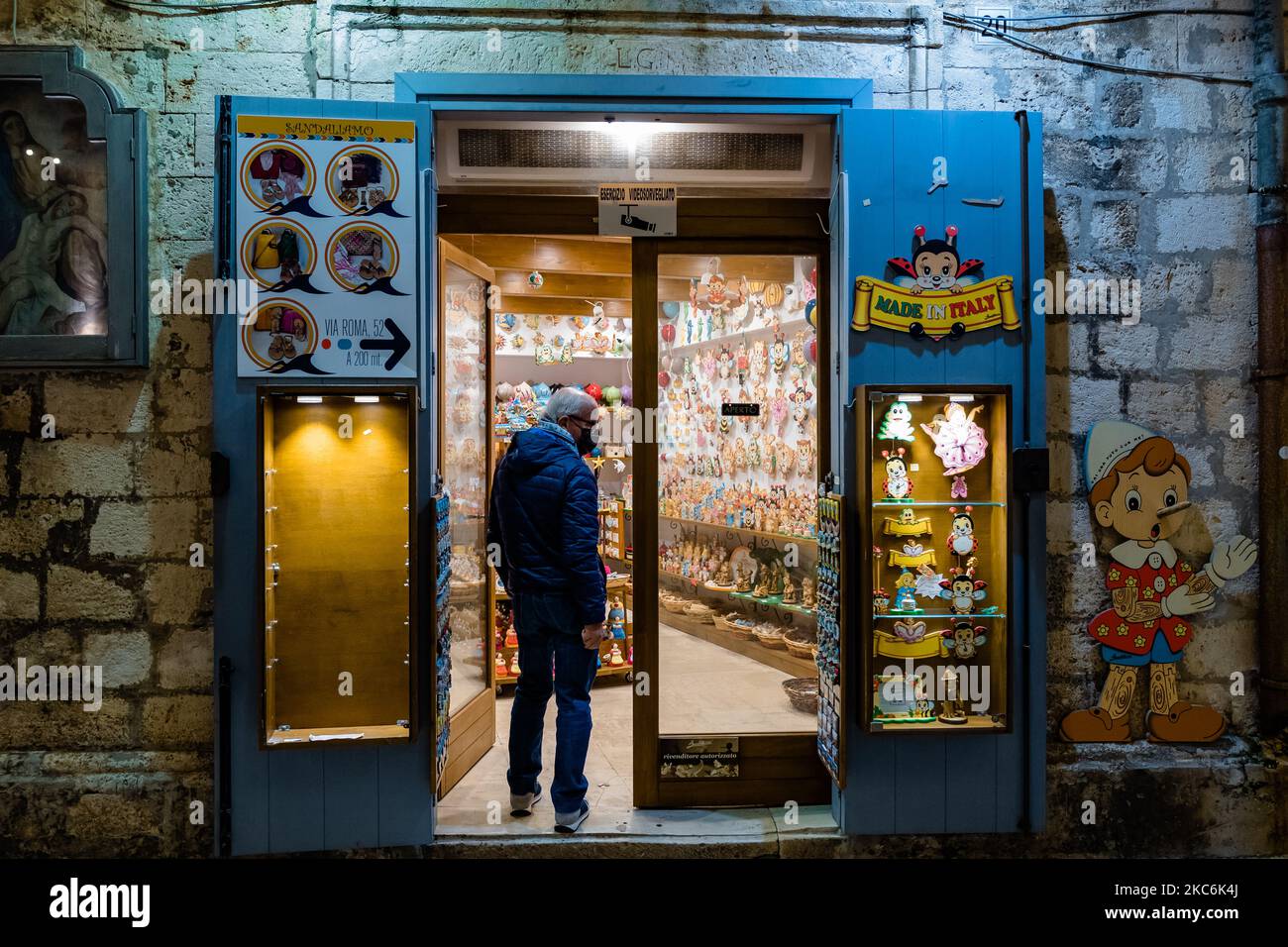 Il proprietario di un negozio di souvenir nel centro storico di Polignano a Mare il 29 dicembre 2020. Polignano si riaccende con le parole di Domenico Modugno. E in particolare con il suo immortale successo, che ha reso famoso in tutto il mondo il cantautore italiano: Volare. Dalla sera del 12 dicembre, i versi della canzone illuminano Via Roma sotto forma di luci, oltre al gioco di luci già attivo a lama Monachile, dando una calda atmosfera natalizia all'affascinante villaggio di Bari che si affaccia sul mare. (Foto di Davide Pischettola/NurPhoto) Foto Stock