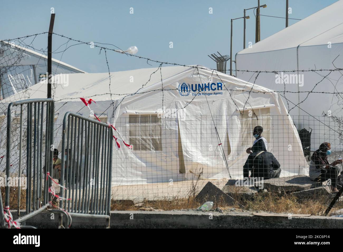 Nuovo campo temporaneo per rifugiati a Kara Tepe - Mavrovouni con grandi tende bianche con il logo UNHCR o UNICEF e richiedenti asilo in attesa di registrazione e forniture come cibo, letti, vestiti ecc come visto dall'ingresso principale custodito. Il nuovo campo recintato è un'ex area militare, campo di tiro dell'esercito ellenico, vicino alla città di Mytilene nell'isola di Lesbos Grecia. Il nuovo campo è stato creato dopo l'incendio del 9 settembre 2020, quando uno dei più grandi campi profughi d'Europa, il campo profughi di Moria (centro di accoglienza, identificazione e registrazione) è stato bruciato. Tutti i residenti, l'asilo cercano Foto Stock