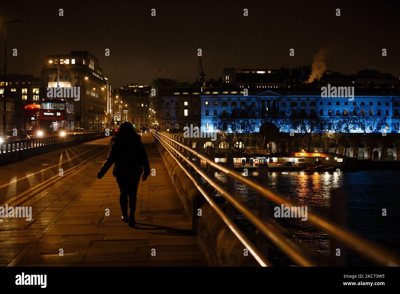 Una donna attraversa Waterloo Bridge mentre Somerset House, illuminata di blu in onore del personale NHS e di altri lavoratori frontline, si trova a Londra, Inghilterra, il 7 gennaio 2021. All'inizio di questa settimana, l'Inghilterra ha iniziato un terzo blocco nazionale del coronavirus, con la preoccupazione delle autorità di far sì che il Servizio sanitario nazionale possa presto essere sopraffatto dai malati di covid-19. Nel frattempo, il primo ministro britannico Boris Johnson ha annunciato oggi che 1,5m persone in tutto il Regno Unito hanno ricevuto almeno una prima dose di un vaccino covid-19, con piani per centinaia di migliaia di vaccinazioni da somministrare ogni giorno a partire dalla metà di questo periodo Foto Stock