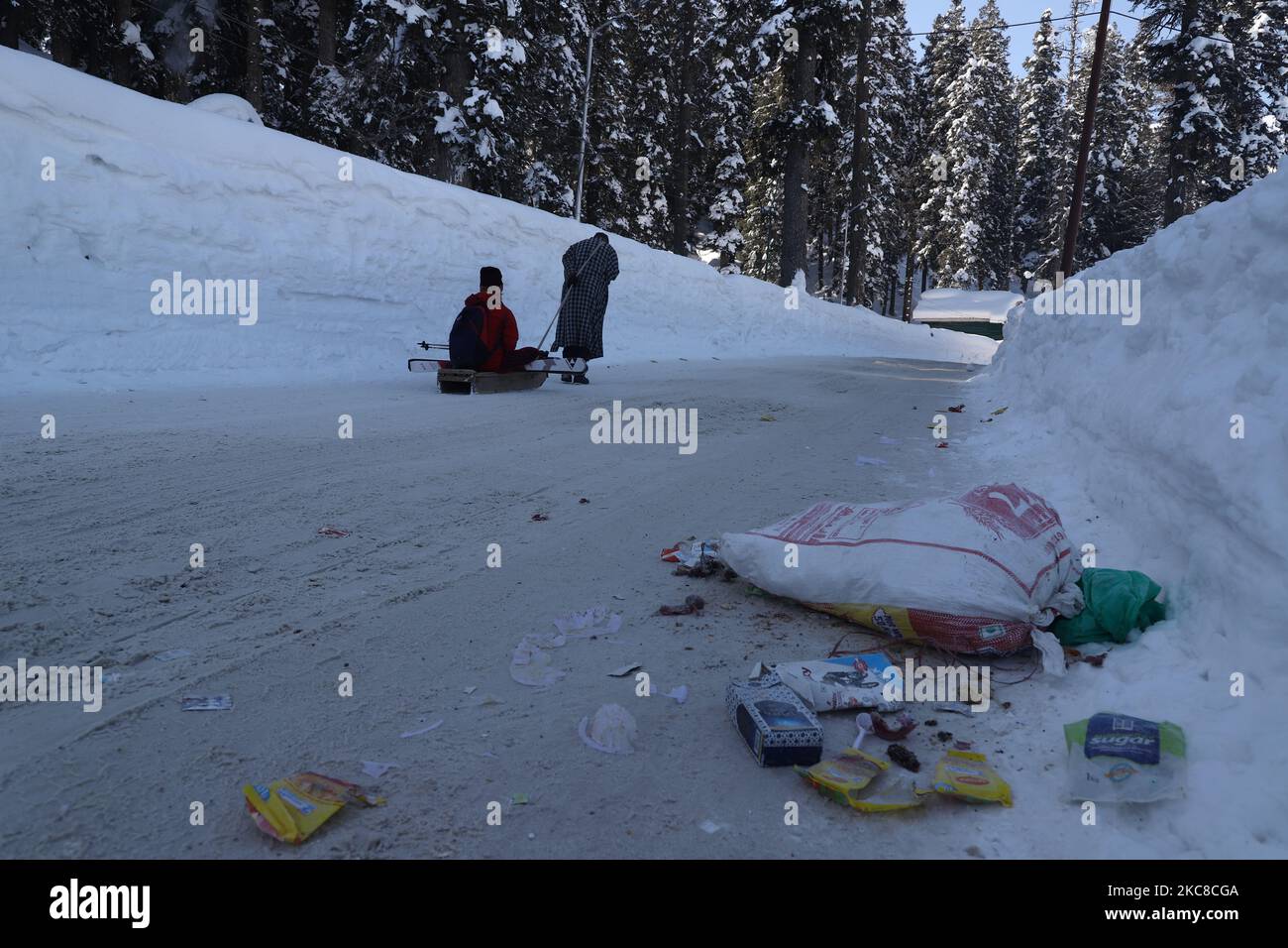 Gli articoli di scarto (involucri alimentari e bottiglie di plastica) di un restautant giacciono sul terreno come un uomo tira una slitta con un turista a Gulmarg nel distretto di Baramulla, Jammu e Kashmir India il 29 gennaio 2021. I turisti sono visti vicino ad un Igloo fatto di neve da un albergatore per attrarre più clienti in Kashmir's Gulmarg, Jammu e Kashmir, India il 29 gennaio 2021. Gulmarg è una città, una stazione di montagna, una popolare destinazione sciistica e un comitato di zona notificato nel distretto di Baramulla di Jammu e Kashmir, India. La città è situata nella gamma PIR Panjal nell'Himalaya occidentale e si trova all'interno dei confini Foto Stock