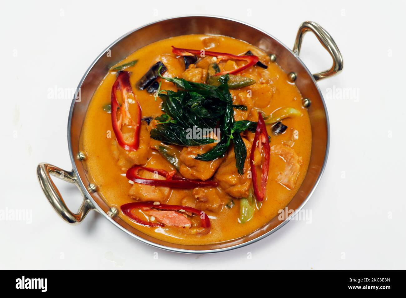 curry di pollo rosso in stile tailandese con peperoncino e basilico in un recipiente da portata con fondo bianco Foto Stock