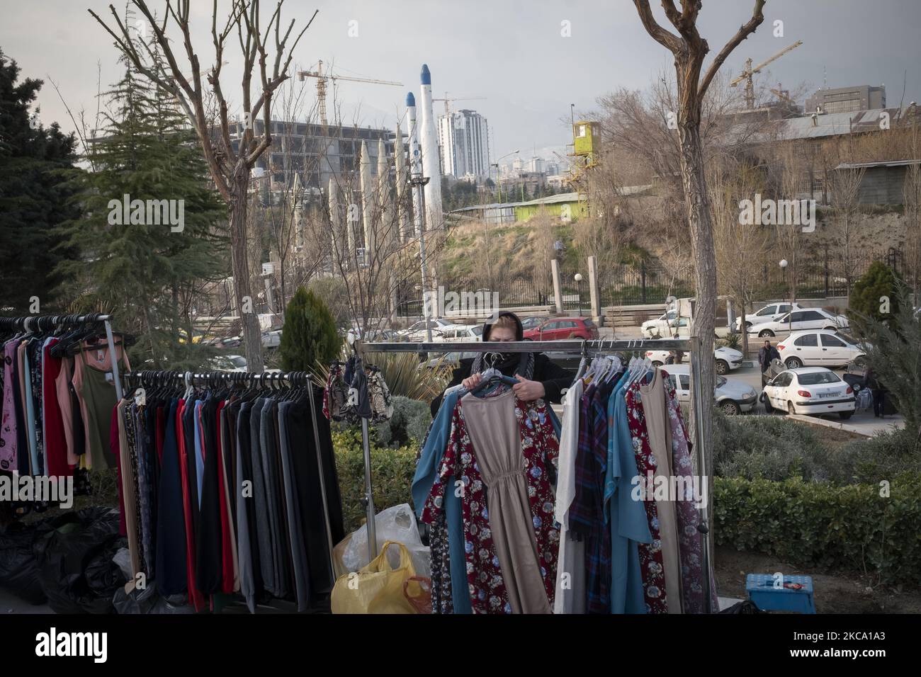 Una donna di vendita iraniana raccoglie abiti dopo una giornata lavorativa nel Parvaneh Friday-Bazaar (mercato), mentre missili iraniani superficie-superficie e due vettori satellitari sono visti sullo sfondo, nel centro di Teheran in mezzo alla nuova epidemia di coronavirus (COVID-19) in Iran, il 26 febbraio 2021. I funzionari iraniani hanno avvertito le persone che il paese è sull'orlo della quarta ondata dell'epidemia di COVID-19 e accadrà se le persone non manterranno protocolli sanitari, distensione sociale e smetteranno di viaggiare verso le altre città. (Foto di Morteza Nikoubazl/NurPhoto) Foto Stock