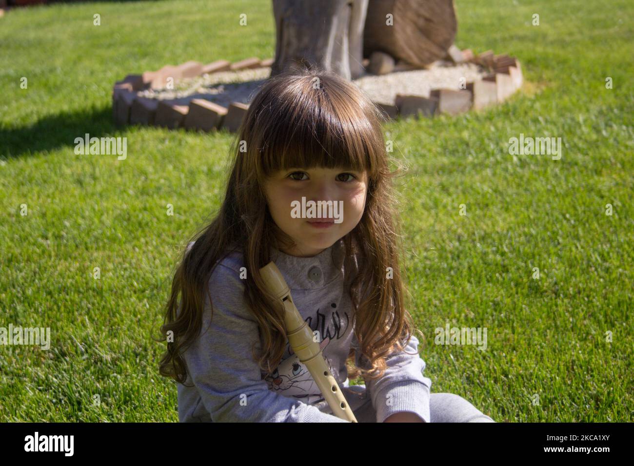 Immagine di un'adorabile bambina sorridente che posa seduta su un prato che tiene un flauto. Giochi educativi per bambini per giocare all'aperto Foto Stock
