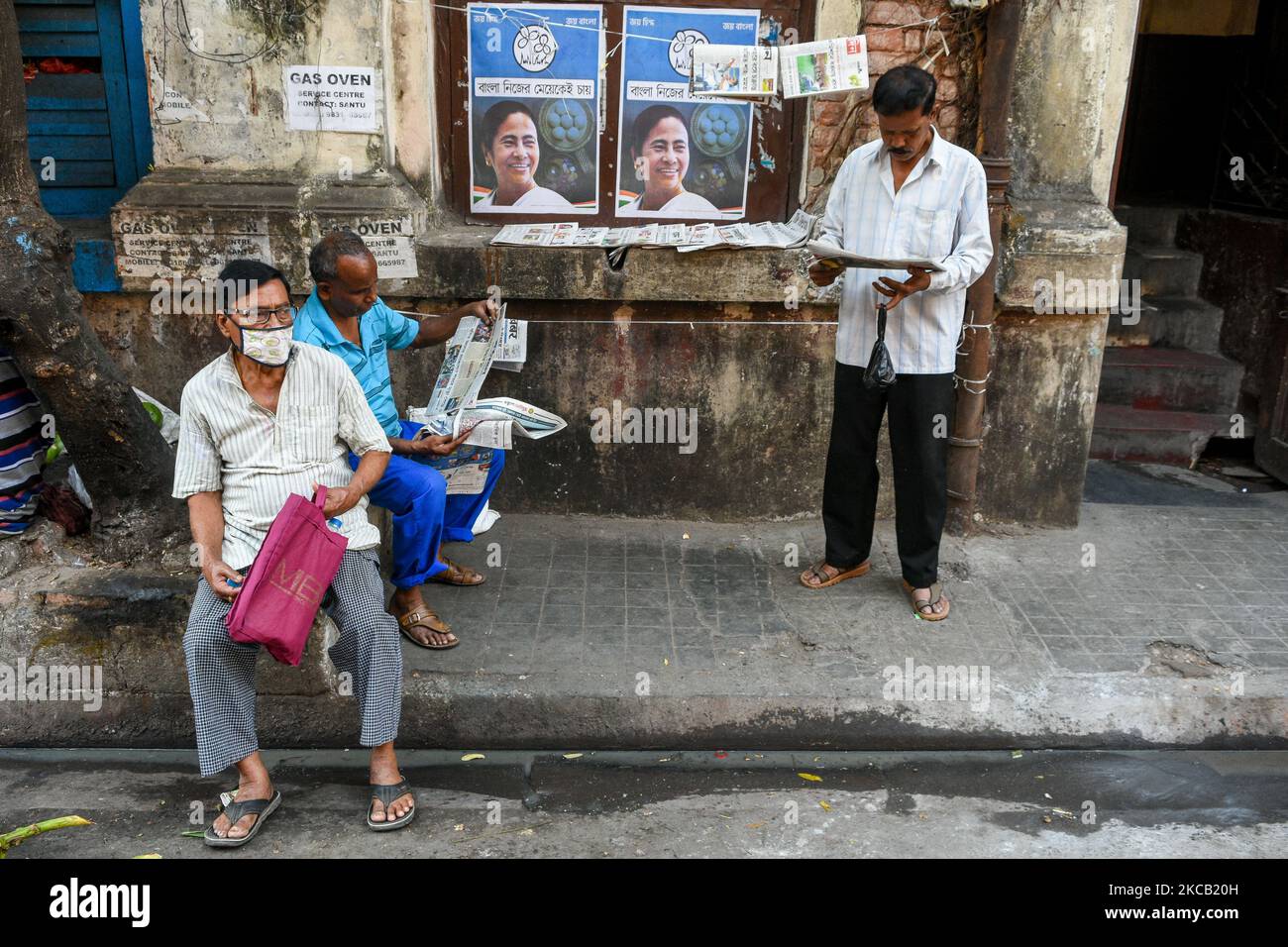 La gente è vista leggere il giornale ad un lato della strada con il manifesto politico della campagna DI CM Mamata Banerjees sul muro di fondo a Kolkata , India , il 17 marzo 2021. (Foto di Debarchan Chatterjee/NurPhoto) Foto Stock