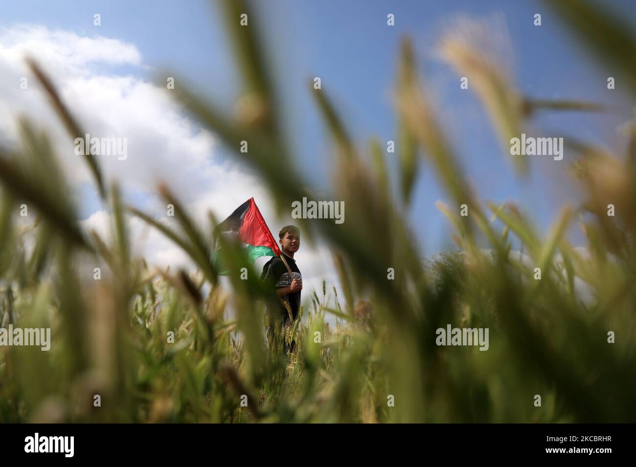 Un giovane palestinese sventola la sua bandiera nazionale durante un evento che segna la Giornata della Terra vicino al confine Israele-Gaza, mentre i raduni di massa previsti per commemorare l'evento sono stati annullati in mezzo alle preoccupazioni circa la diffusione della malattia del coronavirus (COVID-19), ad est di Gaza City, il 30 marzo 2021. (Foto di Majdi Fathi/NurPhoto) Foto Stock