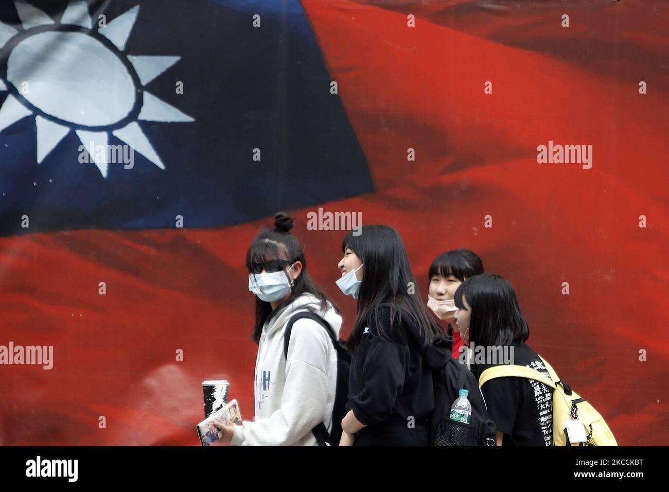 Le persone taiwanesi che indossano una maschera per camminare sul viso  passano una bandiera di Taiwan, in mezzo a tensioni accese con Pechino, a  Taipei, Taiwan, 11 aprile 2021. Con più jet