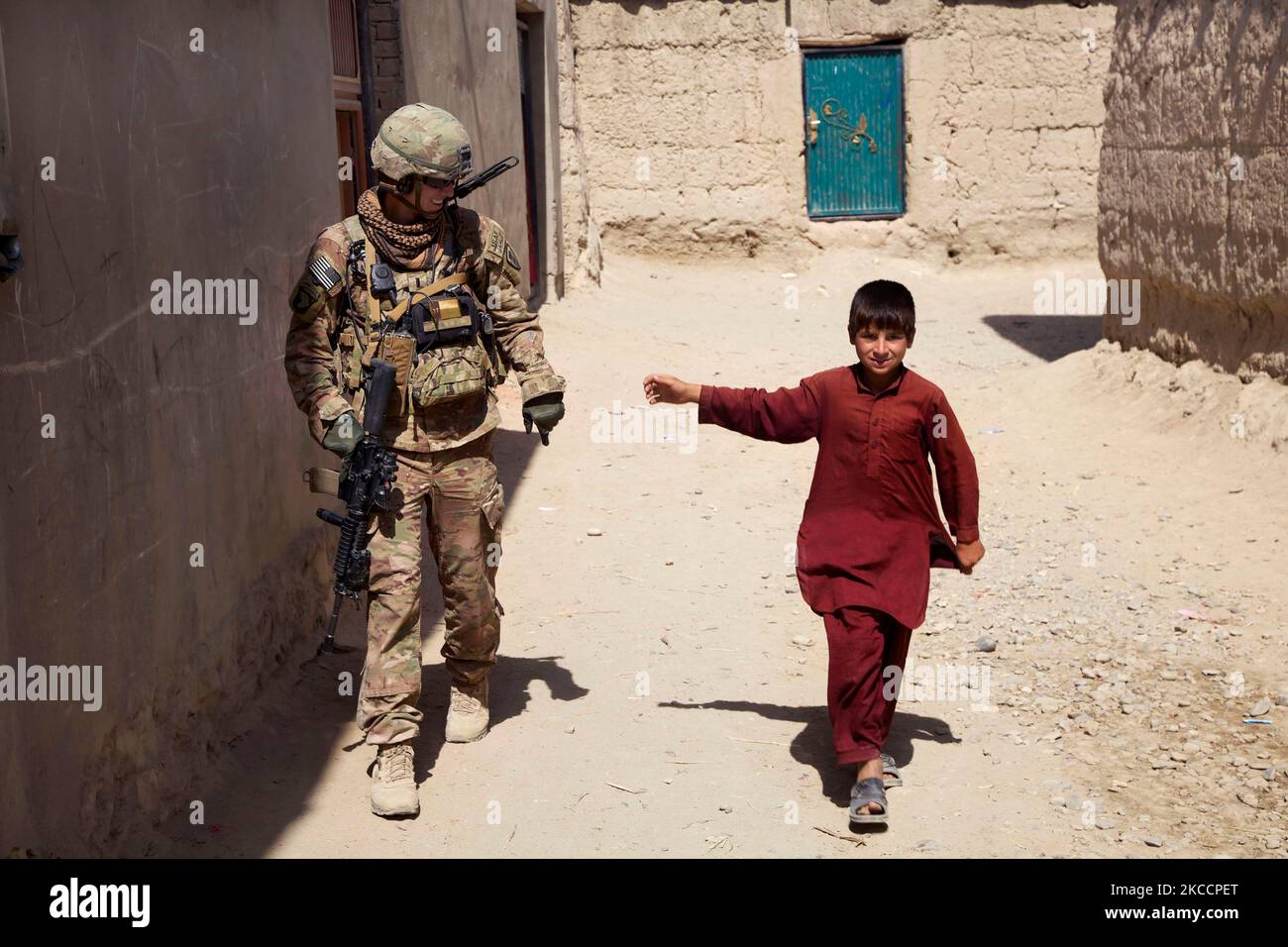 US Army Soldier cammina accanto a un giovane ragazzo mentre in una pattuglia in Afghanistan. Foto Stock