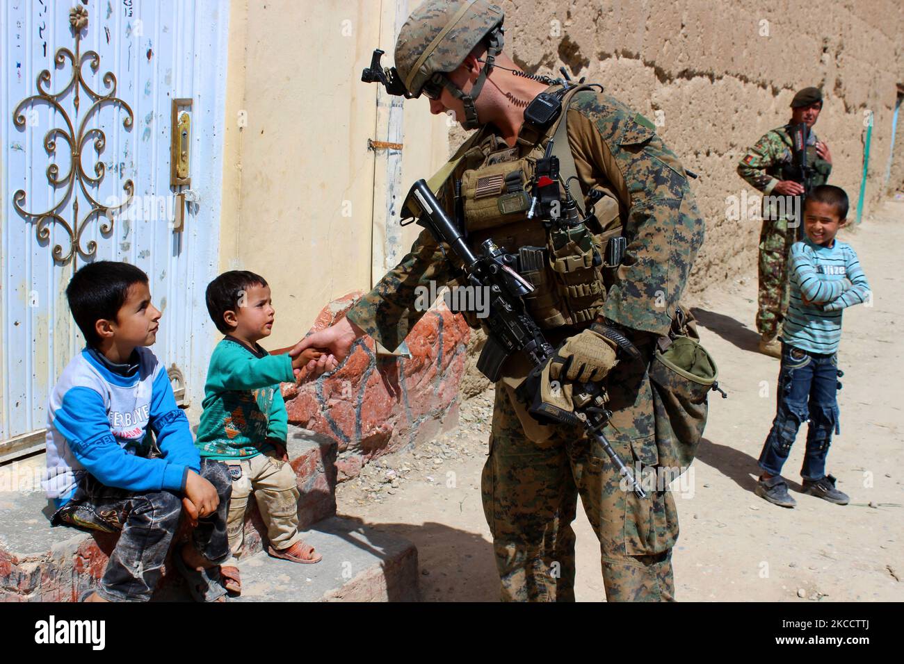 Una Marina statunitense scuote le mani con un bambino afghano. Foto Stock