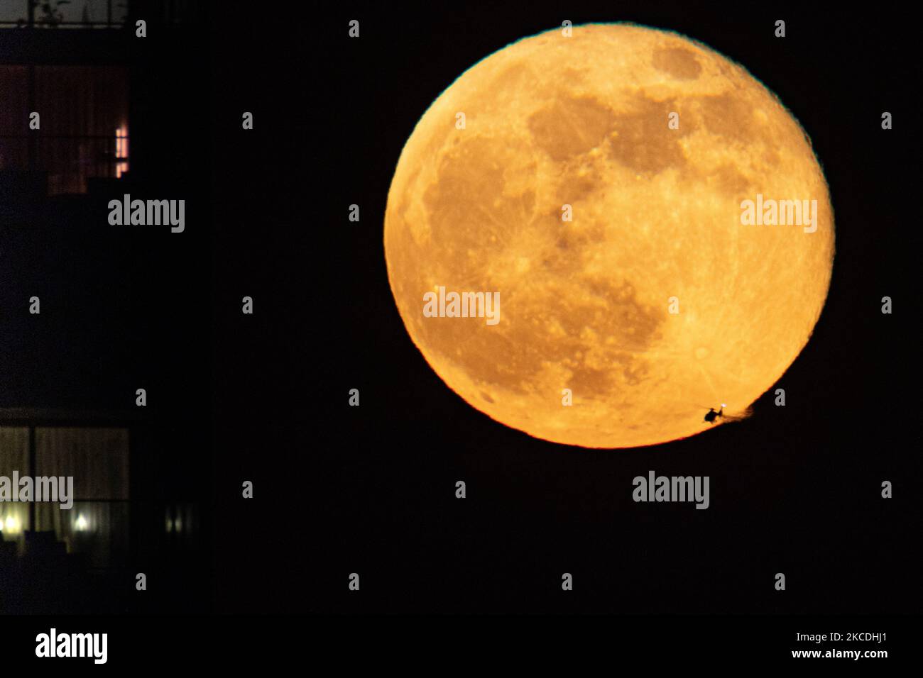 Un elicottero sta passando davanti alla luna. La Luna piena o la Superluna Rosa o la Luna Super Rosa del 2021 aprile, come si vede dalla città olandese, Eindhoven, Paesi Bassi il 27 aprile 2021, che si erge sopra l'orizzonte dietro gli edifici di colore rosso. La luna piena super è più grande e più luminosa nel cielo perché è più vicina alla Terra., 14 per cento più grande e 30 per cento più luminoso di una dimensione e luminosità comuni di una luna normale. Il nome della Luna Rosa è legato alla fioritura primaverile dei fiori. Altri nomi satellite naturale della Terra in orbita intorno al pianeta e satellite più grande nella S Foto Stock