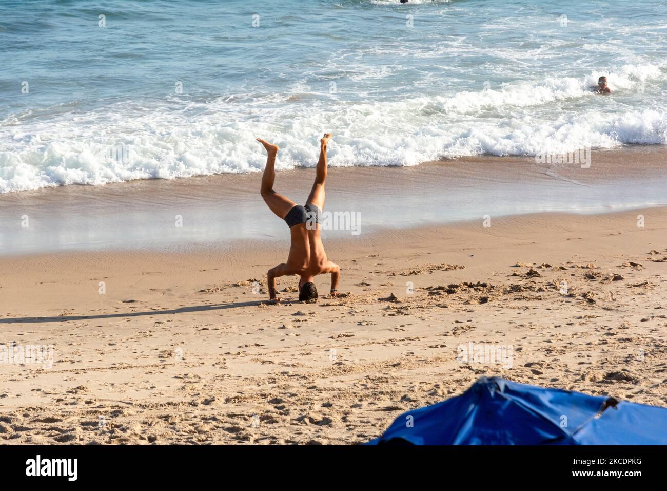 Un uomo fa esercizi di yoga sulla sabbia di Farol da barra spiaggia a Salvador, Brasile, mentre altre persone a piedi Foto Stock