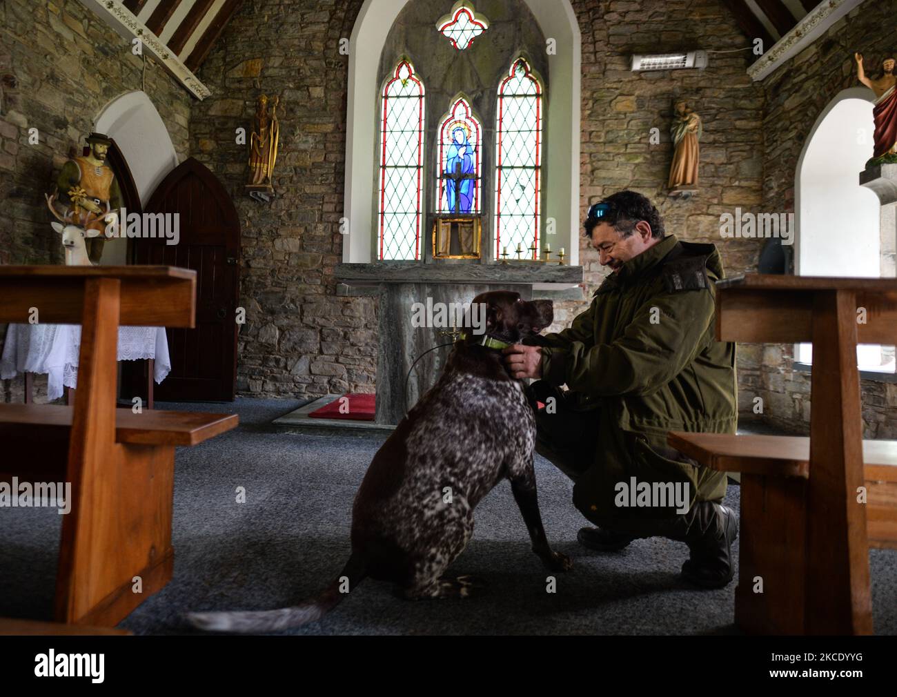 Padre Krzysztof Sikora con il suo cane 'Rambo' visto all'interno della Chiesa di Ballynahinch, a Emlaghdauroe, Connemara. Questa ex chiesa della Chiesa d'Irlanda, datata 1865, ora conosciuta come St. Hubert, il santo patrono dei cacciatori, è situata nel paesaggio più spettacolare di montagne, palestre e laghi. Geograficamente, la parrocchia di Roundstone è considerata la più grande parrocchia d'Irlanda e si estende dalle spiagge di Gurteen ai Monti Twelve Bens e Mám Tuirc. Fino agli anni '1990s la parrocchia era servita da tre sacerdoti, ora CE n'è una sola che si occupa di cinque chiese. L'attuale Parroco, un polacco nato Padre Krzyszt Foto Stock