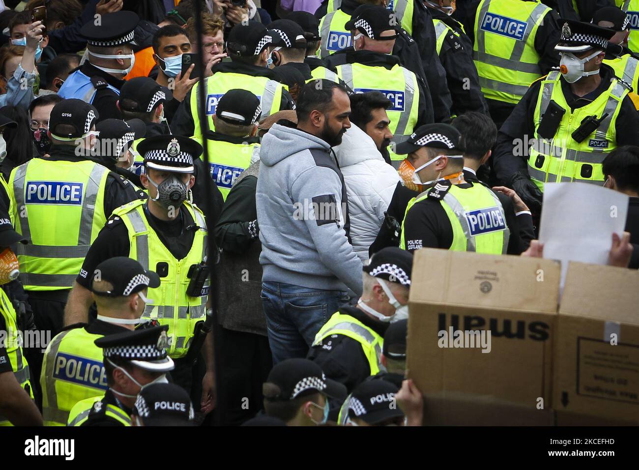 Due uomini (giacche grigie e bianche) sono portati via dopo essere stati rilasciati dalla custodia degli uffici domestici britannici dopo che i manifestanti hanno bloccato un furgone di applicazione dell'immigrazione dell'ufficio domestico britannico dopo che un tentativo di raid è stato effettuato il mattino a Kenmure Street in Pollokshields il 13 maggio 2021 a Glasgow, Scozia. (Foto di Ewan Bootman/NurPhoto) Foto Stock