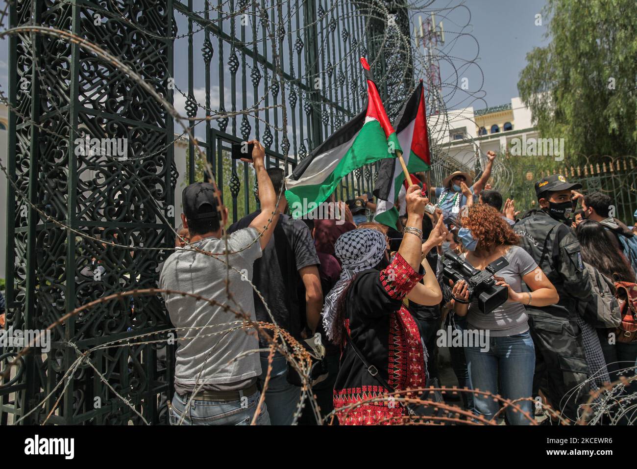 I manifestanti alzano le bandiere palestinesi e sollevano pugni davanti alla porta del Parlamento tunisino dopo aver rimosso il filo spinato, durante una manifestazione svoltasi di fronte all'edificio del parlamento tunisino nella città di Bardo Tunisi, in Tunisia, il 18 maggio 2021; Chiedere l'adozione da parte del parlamento di una legge che criminalizzi tutte le forme di normalizzazione delle relazioni con Israele. I dimostranti hanno protestato anche contro gli attacchi aerei israeliani sulla striscia di Gaza e contro le violazioni israeliane nei territori occupati in Palestina, in particolare nel quartiere palestinese Sheikh Jarrah, a Jerus orientale Foto Stock