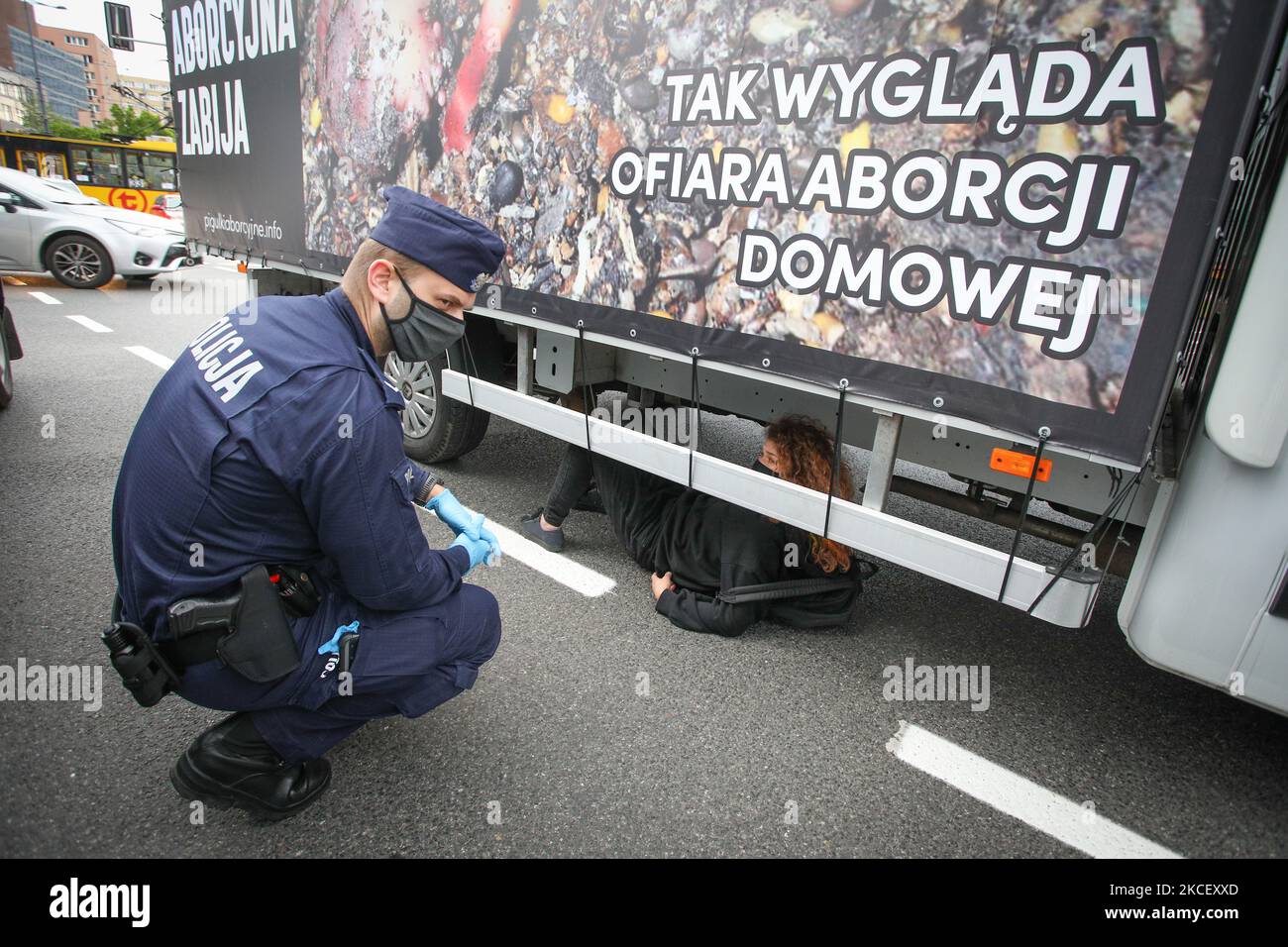 Una donna si trova sotto un furgone per bloccarlo a Varsavia, Polonia, il 19 maggio 2021. Gli attivisti anti-aborto in un furgone che mostra immagini grafiche di feti abortiti sono stati fermati da attivisti pro-scelta nel centro di Varsavia, Polonia. L'attivista Weronika, ventenne, si è seduto sulla strada di fronte all'autobus, in quanto si trovava all'uscita della trafficata rotonda ONZ. Gli autisti dell’autobus suonavano un forte allarme attraverso gli altoparlanti del furgone nel tentativo di scongiurare l’attivista. Altre due donne, Magda e Lu, si accovacciarono sotto l'autobus. Diverse dozzine di polizia arrivarono presto sulla scena e agli attivisti furono inflitte multe wh Foto Stock