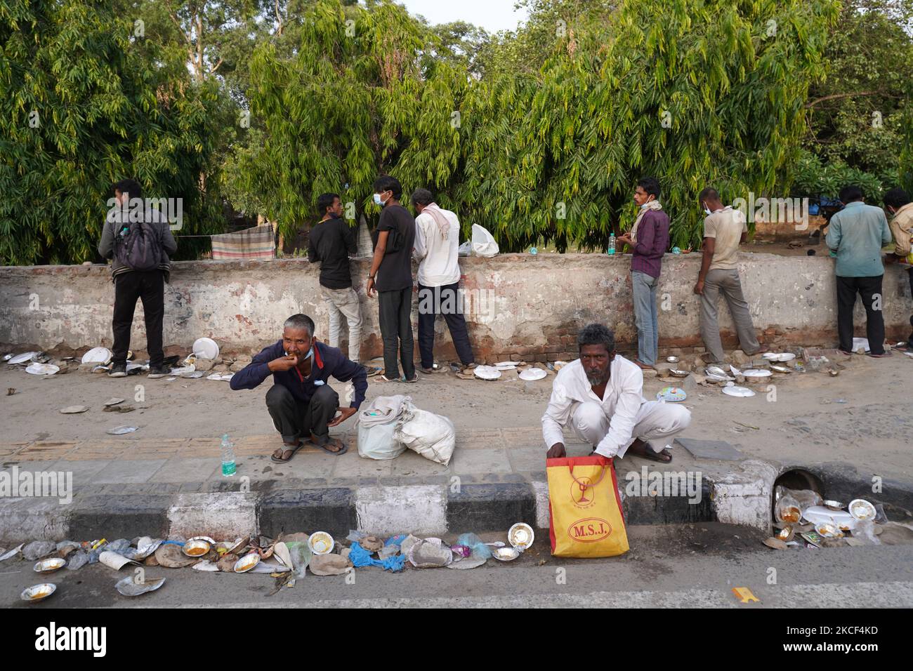 I senzatetto e i lavoratori salariali quotidiani, che lottano per trovare lavoro tra le restrizioni imposte per frenare la diffusione di Covid-19, mangiano il cibo distribuito da volontari lungo una strada il 23 maggio 2021 a Nuova Delhi, India. (Foto di Mayank Makhija/NurPhoto) Foto Stock