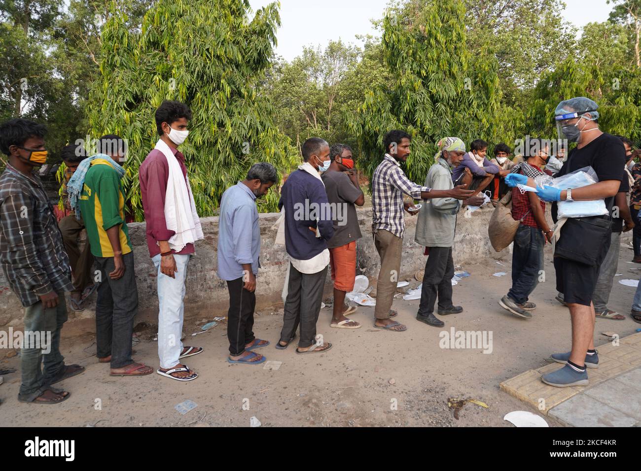 I senzatetto e i lavoratori salariali quotidiani, che lottano per trovare lavoro in mezzo a restrizioni imposte per frenare la diffusione di Covid-19, ottenere maschere gratuite come coda fino a ricevere cibo distribuito da volontari lungo una strada il 23 maggio 2021 a Nuova Delhi, India. (Foto di Mayank Makhija/NurPhoto) Foto Stock