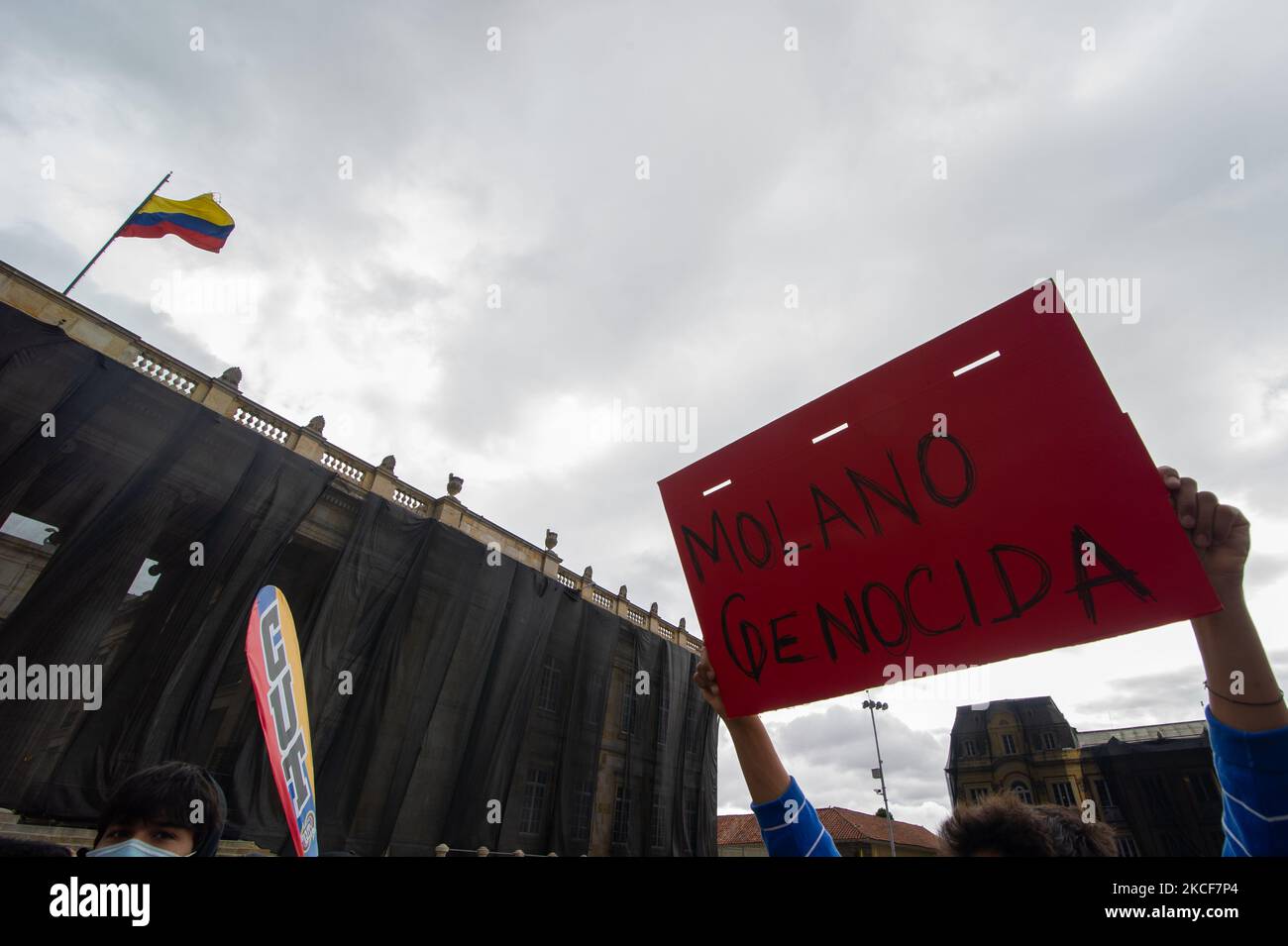 Un dimostratore ha in mano un segno che recita "genocidio Diego Molano" con l'edificio del congresso colombiano alle spalle mentre la gente si riunisce in Plaza de Bolivar di fronte al Campidoglio del Congresso per sostenere la mozione di censura al ministro della Difesa colombiano Diego Molano dopo almeno 45 morti in casi di brutalità della polizia durante Le proteste contro il governo contro le riforme fiscali e sanitarie e la brutalità della polizia si sono evolute in Colombia nelle ultime settimane, a Bogotà, in Colombia, il 24 maggio 2021. (Foto di Sebastian Barros/NurPhoto) Foto Stock