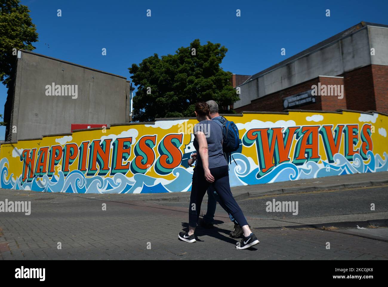 Una coppia passa davanti a un nuovo murale 'Happiness Waves' nel centro di Dún Laoghaire. Dal giugno 22nd, le strade e le corsie di Dún Laoghaire si illuminano con una serie di opere d'arte di strada nell'ambito del progetto Dún Laoghaire Anseo. Domenica 27 giugno 2021 a Dublino, Irlanda. (Foto di Artur Widak/NurPhoto) Foto Stock