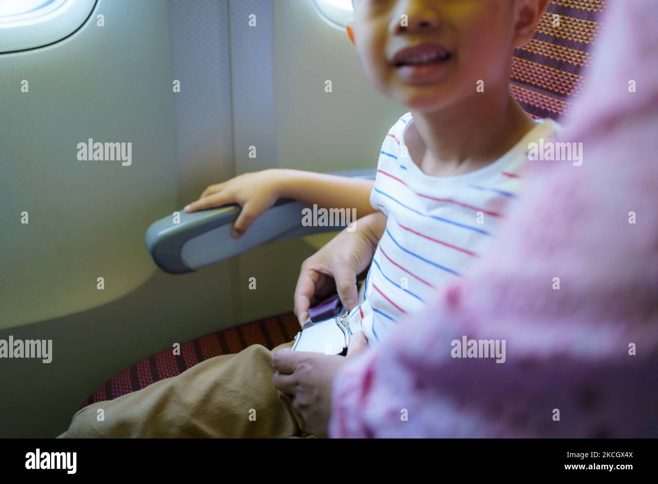 Bambino asiatico in cabina di volo allacciare la cintura di sicurezza viaggio vacanza con la madre Foto Stock
